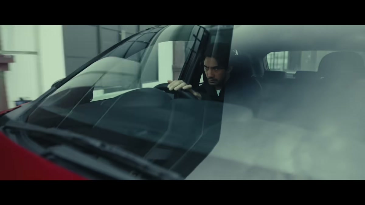 A driver framed through the windshield of a red Honda, hand on the wheel, in a moody industrial setting, from the Start with Trust digital film series.
